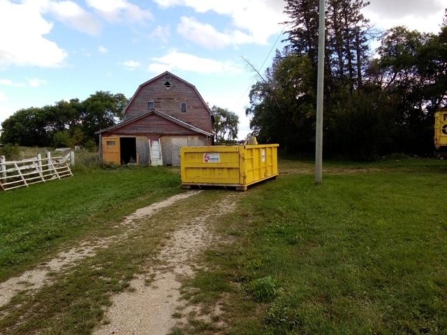 A yellow garbage bin located in a farm yard in front of an old barn